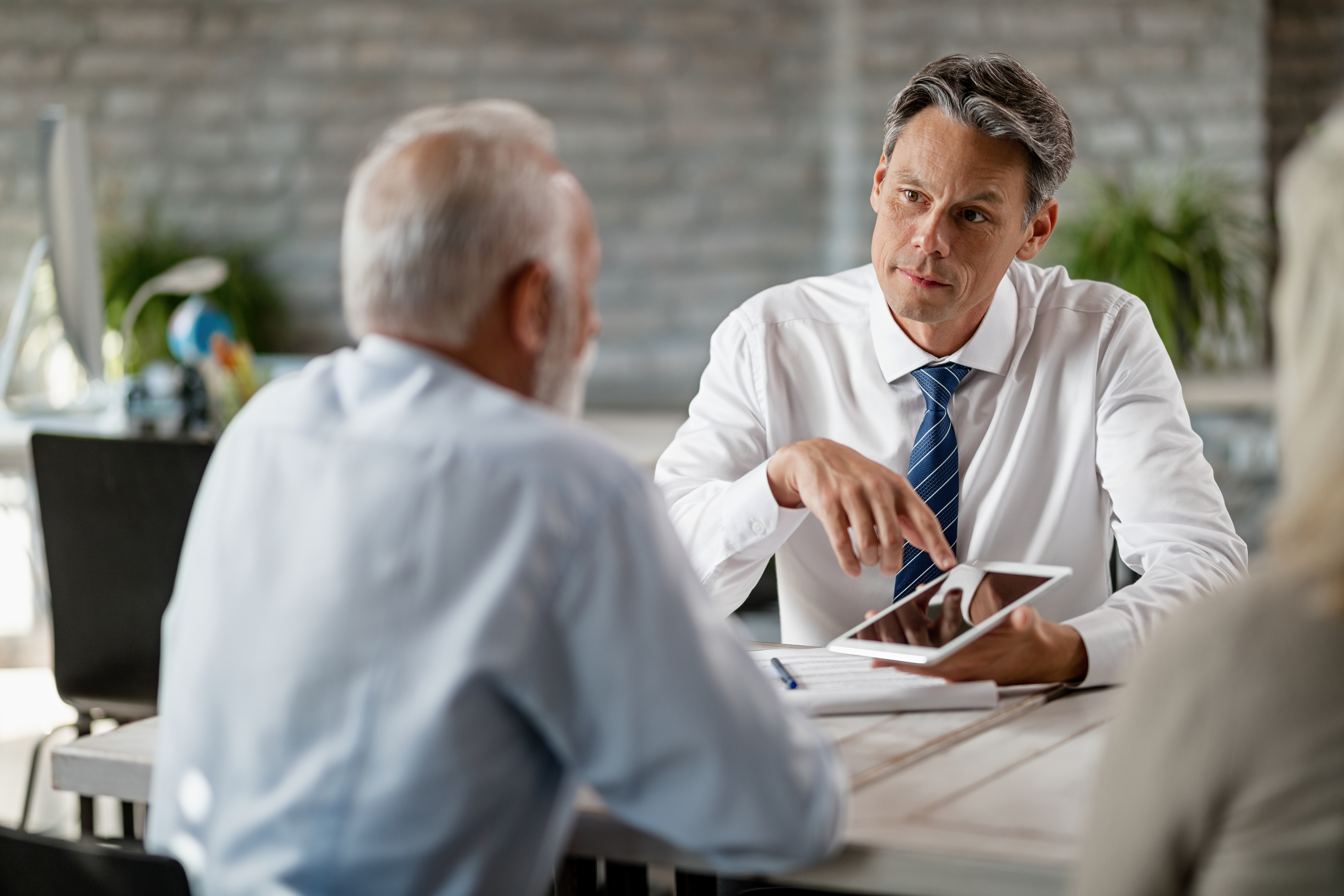 Financial advisor using digital tablet on a meeting with senior clients.